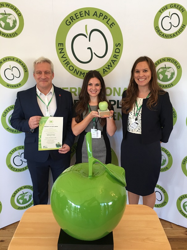 Accepting the Green Apple Award. Three people stand behind a large apple sculpture. Two women and one man.