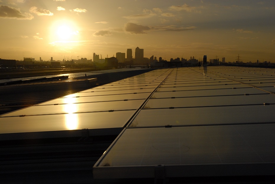 An image of London at sundown. The solar panels are in the foreground with a panoramic view of East London in the background