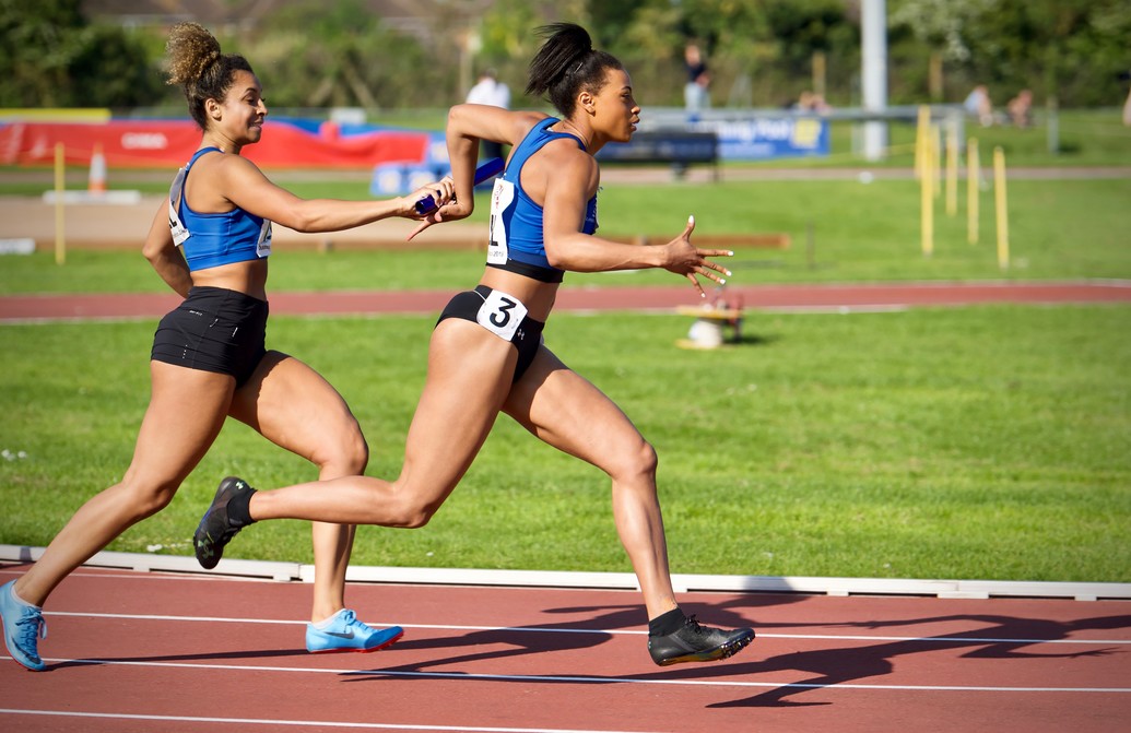 Two runners in a relay race passing the baton.