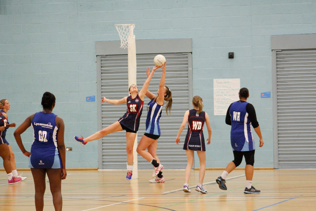 Netball game being played. One player is trying to shoot a hoop and is being blocked by her oponent.
