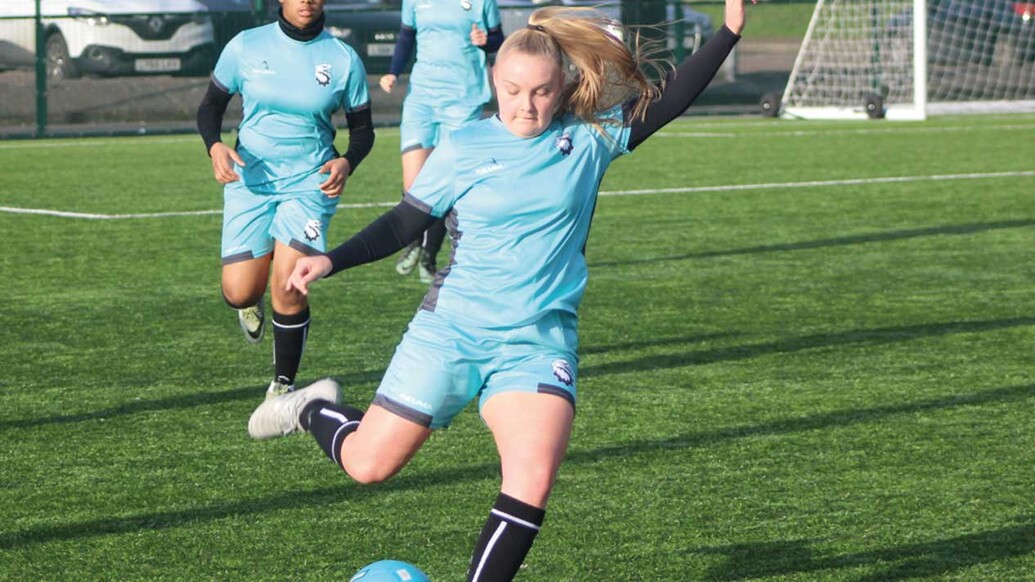 Female footbal player mid kick. Her team mates are positioned behind her.