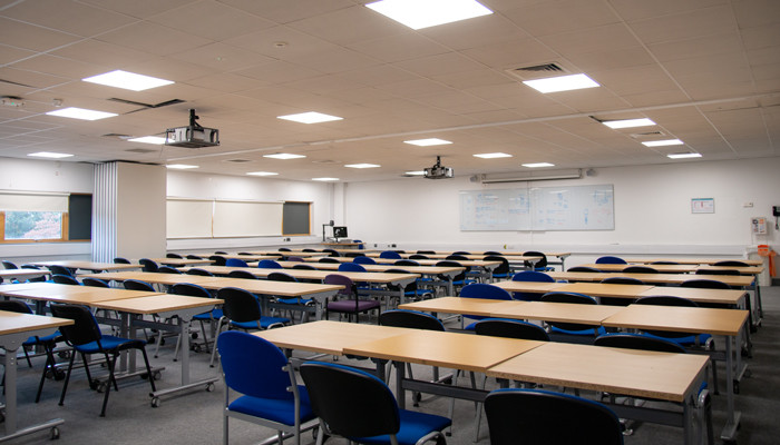 Main conference room with rows of desks and blue chairs. At the front is a whiteboard,