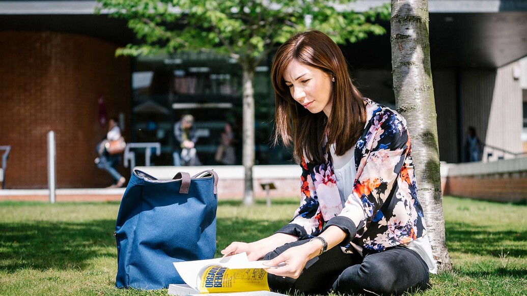 Female sitting on grass outdoors reading a textbook